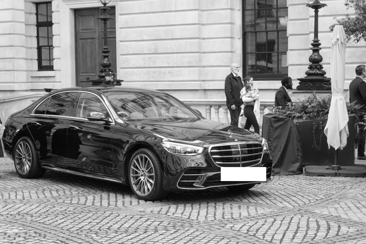 Black executive saloon with a security detail outside a private venue